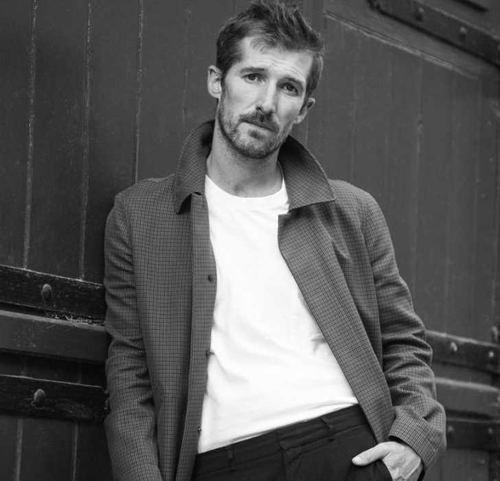 Picture of Gwilym Lee posing for a photo by putting his left hand in pocket with black and white photo